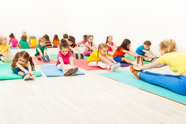 Portrait of female coach teaching kids doing warming-up during gymnastics